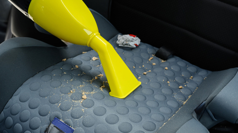 Person vaccuuming the seat of a car.