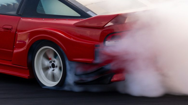 Close-up of Nissan 240SX rear-left fender while drifting with tire smoke visible