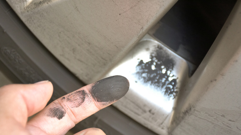 Finger with black brake dust on it and dirty rim in background