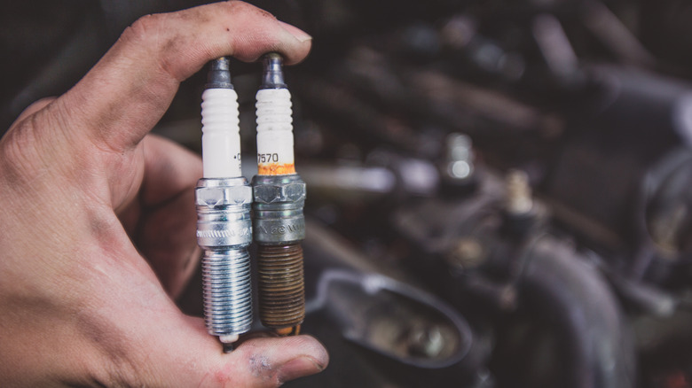 A mechanic holding a used, dirty spark plug and a new, clean spark plug next to each other