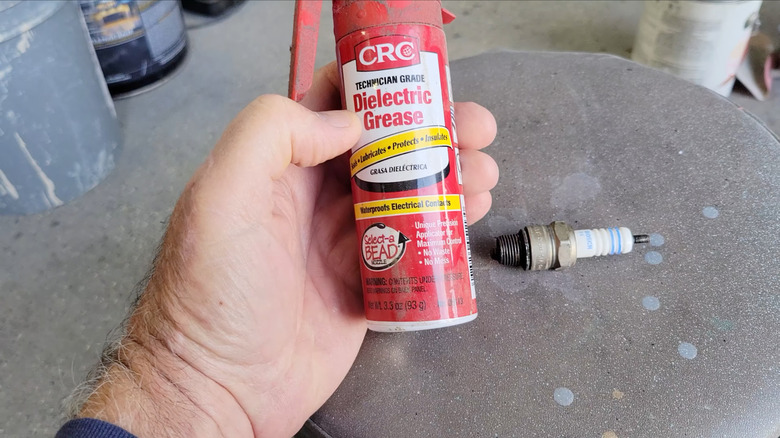 A person holding a can of CRC dielectric grease next to a new spark plug on a makeshift work bench
