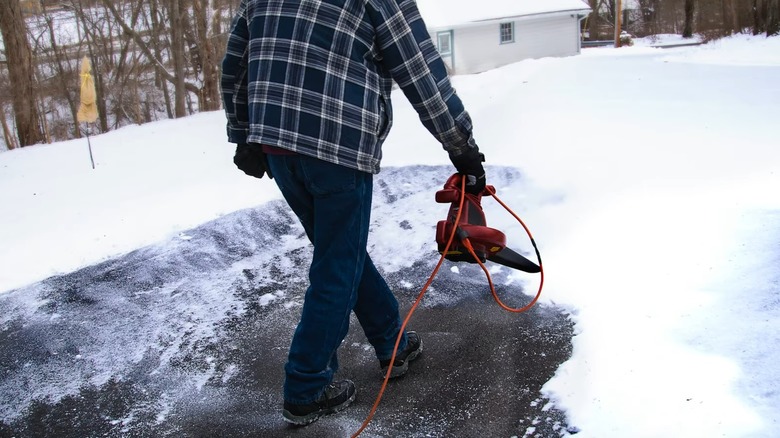 A person using a leaf blower to remove snow from a driveway.