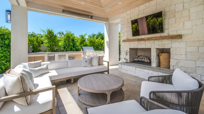 An outdoor living area with couches, a grill, a fireplace, and a TV