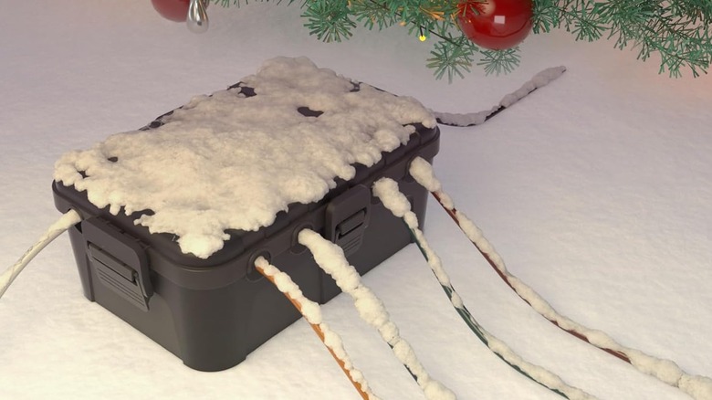 An outdoor storage box for cables covered in snow near a tree decorated for Christmas