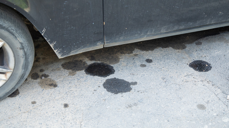 A close-up of a dirty car and a few oil stains on the ground