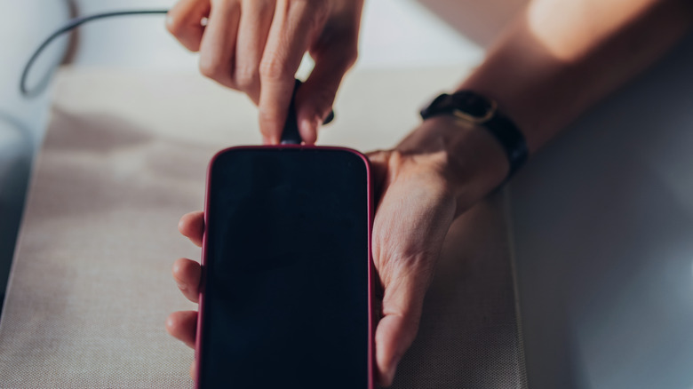 Hand plugging a charging cable into a phone