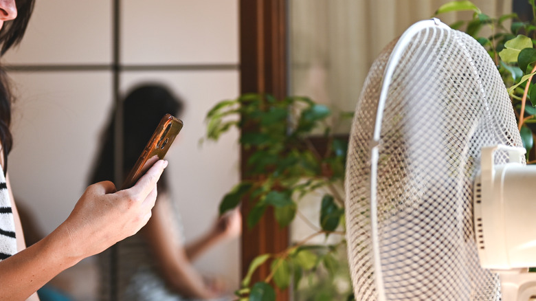 Woman holding phone in front of electric fan