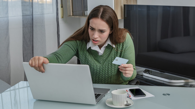 A woman holding a credit card and her laptop on table