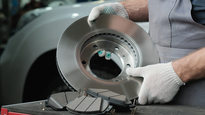 A mechanic preparing a brand new brake rotor for installation, unidentified white car in the background