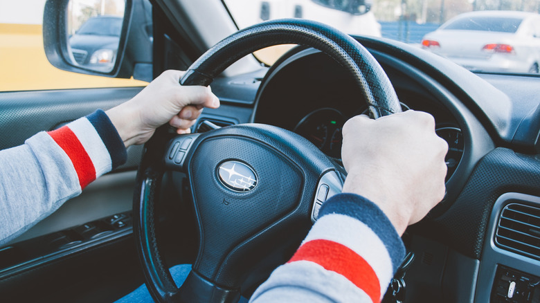 Person driving Subaru with hands on wheel