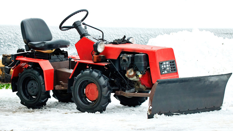 Red snow plow tractor equipped with brush machine cleaning snowy driveway outdoors