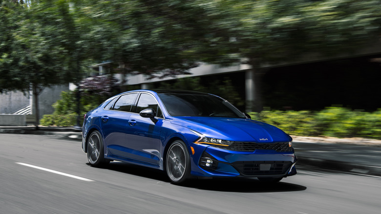 2024 Kia K5 driving on urban road, front-right 3/4 view