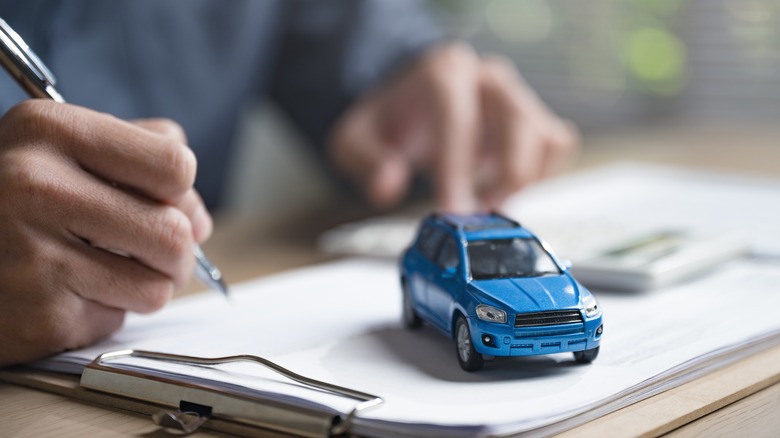 Close-up of person filling out document on clipboard with crossover vehicle paperweight