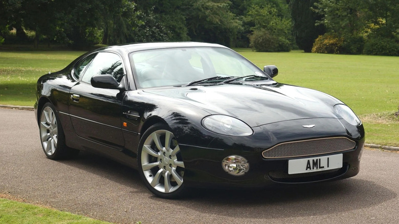 Black Aston Martin DB7 Vantage parked on a country driveway, featuring elegant British grand tourer styling with distinctive mesh grille and alloy wheels.