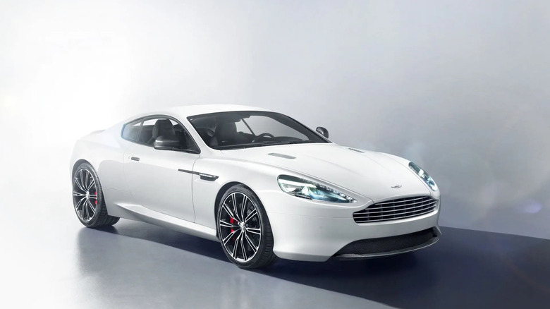 White Aston Martin DB9 sports coupe in a studio setting, highlighting its sleek modern design, LED headlights, and luxury performance aesthetics.
