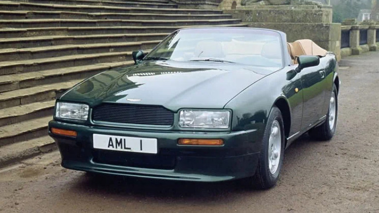 Classic green Aston Martin Virage Volante convertible parked beside stone steps, showcasing luxury British car design.