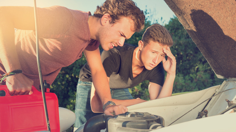 Young men looking at the engine of a broken down car.