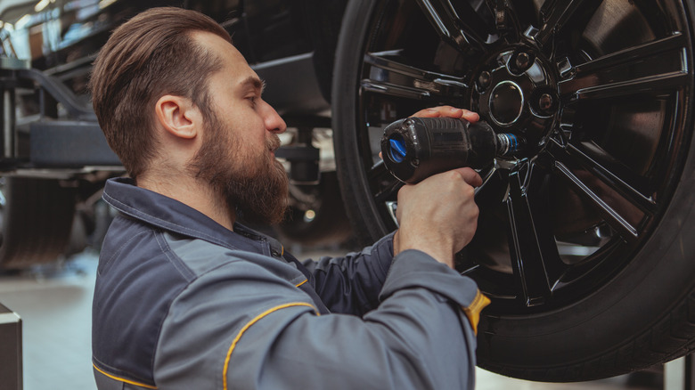 Bearded male car mechanic torquing the lug nuts of a wheel of a lifted car at his garage