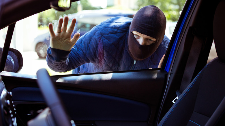 Unrecognizable man wearing balaclava breaking into the car.