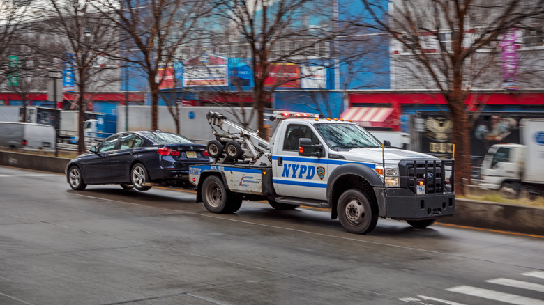 New York Police Department tow truck towing a car down the street.