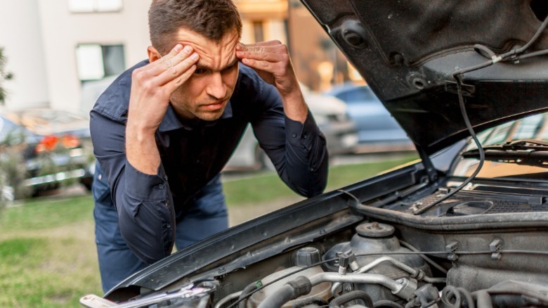 A frustrated person looking at their engine after being unable to start their car