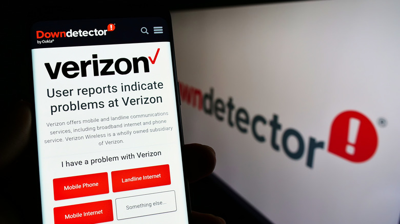 Verizon website on smartphone held alongside display showing Down Detector website
