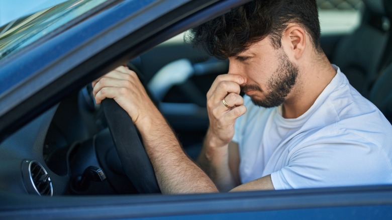 A driver holding their nose because of a bad air conditioner smell