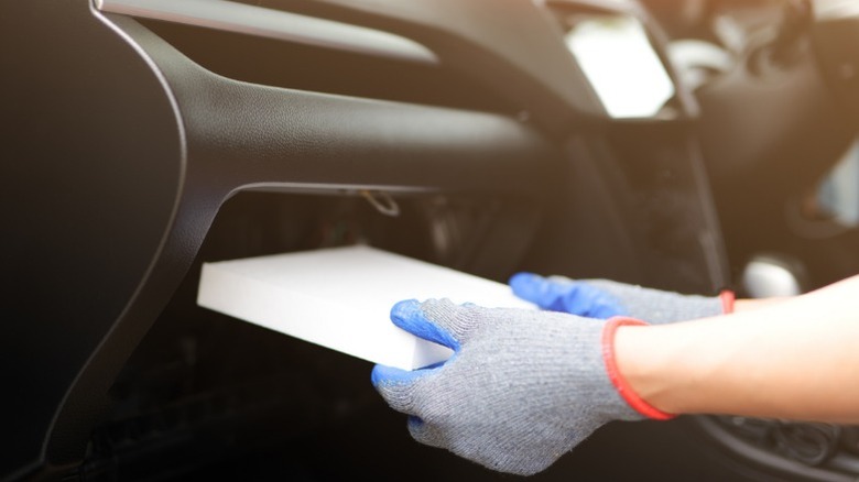A person wearing gloves while replacing their car's cabin air filter