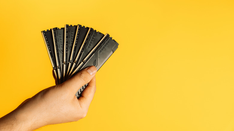 Hand holding several sticks of RAM on a yellow background