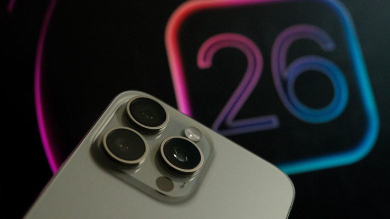 A recent iPhone Pro model with the iOS 26 logo in the background at an announcement event