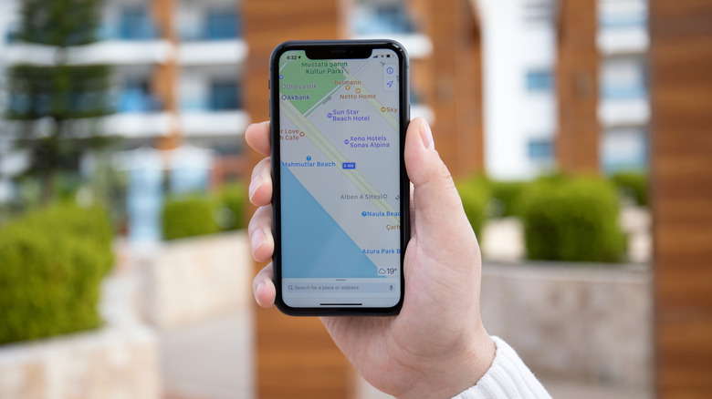 A man's hand holding an iPhone 11 with Apple map on the screen.