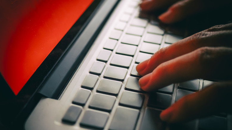 A computer hacker works at an ominously red laptop screen.