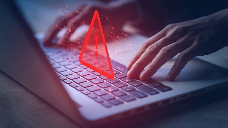 Warning sign on a laptop keyboard, hands typing