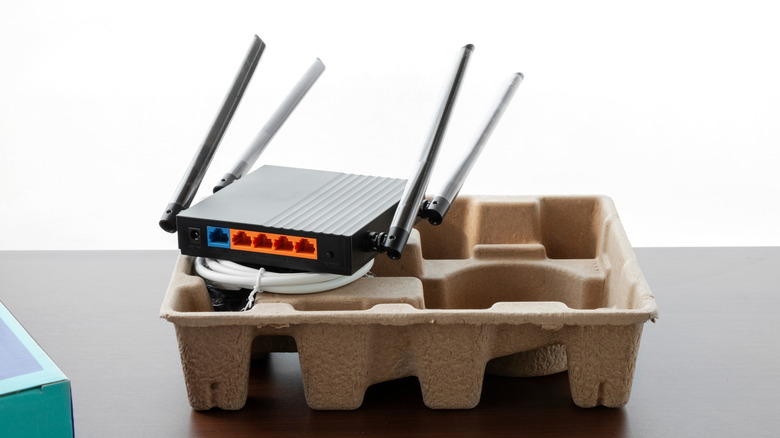 A black router half-unboxed on top of some packaging with a bundled white ethernet cable.