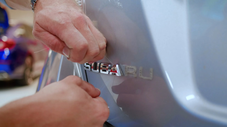 A person removing the Subaru wordmark off a trunk lid using string