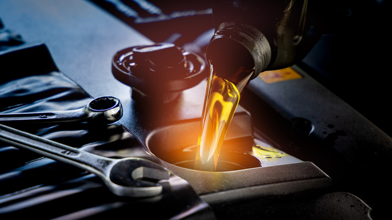Close-up of oil poured into an engine with a pair of wrenches resting nearby