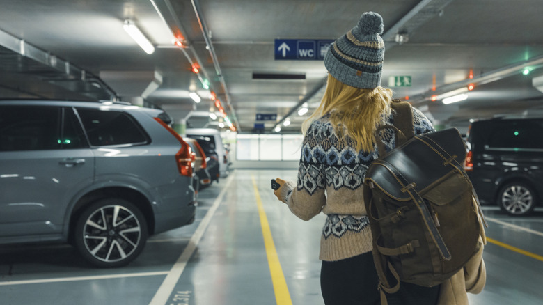 Rear view of pedestrian with key fob inside of a parking garage showing backed-in vehicles