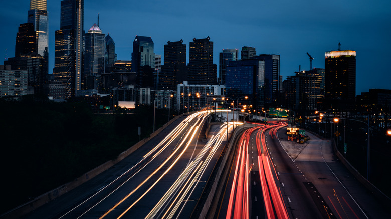 A beautiful vibrant view of the city of Philadelphia, Pennsylvania at nighttime, the lights of the skyscrapers and building glowing brightly. Long exposure photo, with the car tail lights and head lights creating light trails.