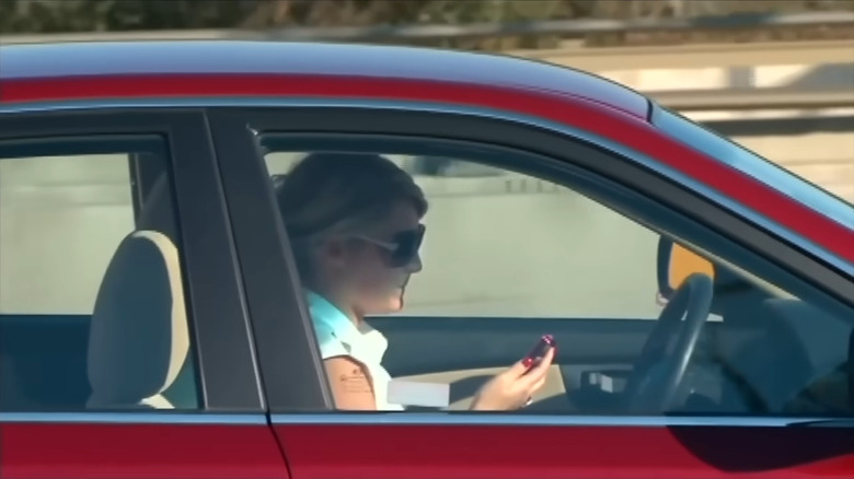 Woman driver holding her phone in her hand, head tilted slightly down while looking at the screen.