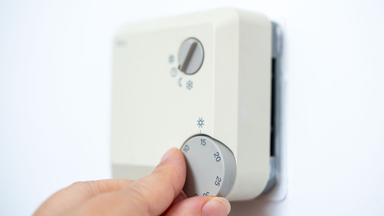 Person adjusts a thermostat on a wall.