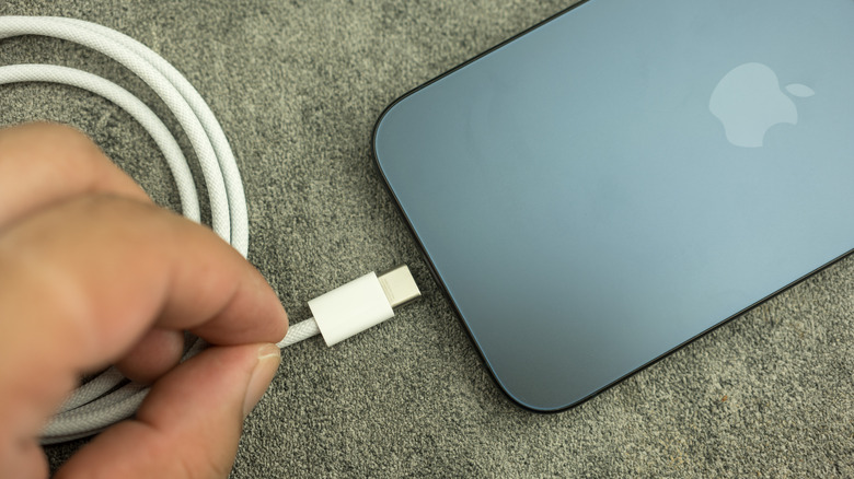 Hand getting ready to plug in charger to silver iPhone