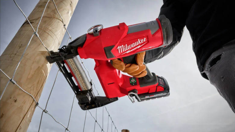 Milwaukee fencing stapler in gloved hand pressed against fence post