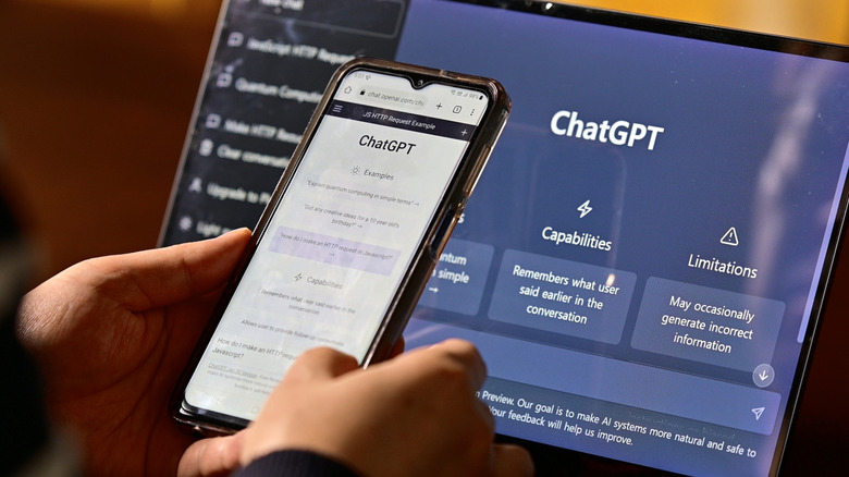 Hands holding a smartphone displaying ChatGPT with a laptop also displaying ChatGPT in the background