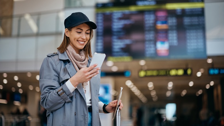 A smiling woman using her phone at an airport