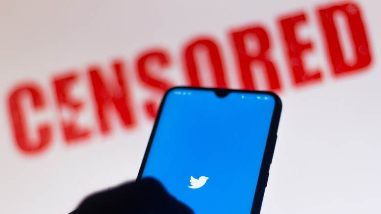 Twitter on phone in front of censored sign