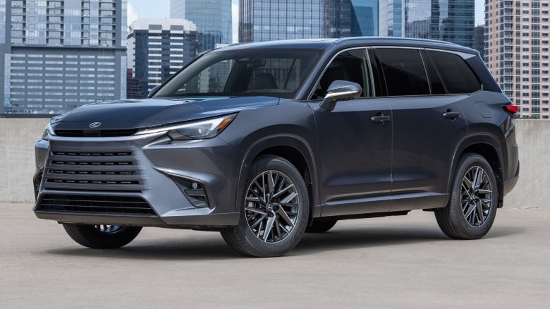 A black Lexus TX 350 Premium parked on a paved surface with a cityscape in the background