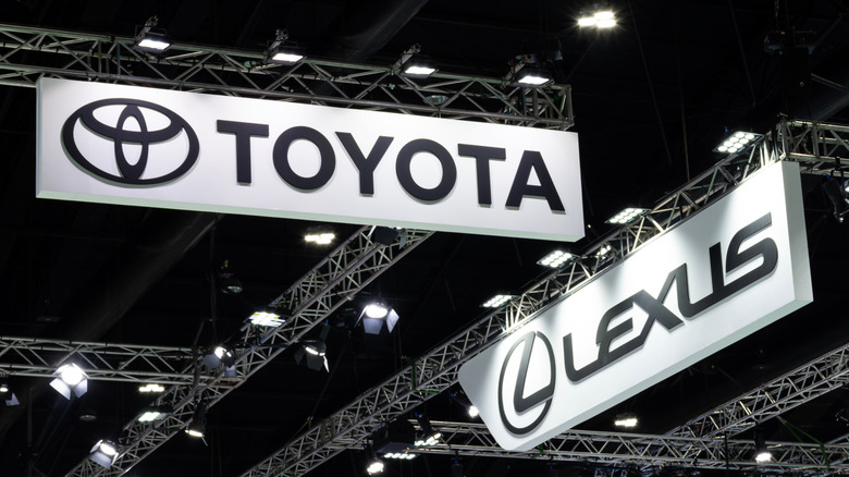 White Toyota and Lexus signs next to each other, hanging off of metal scaffolding.