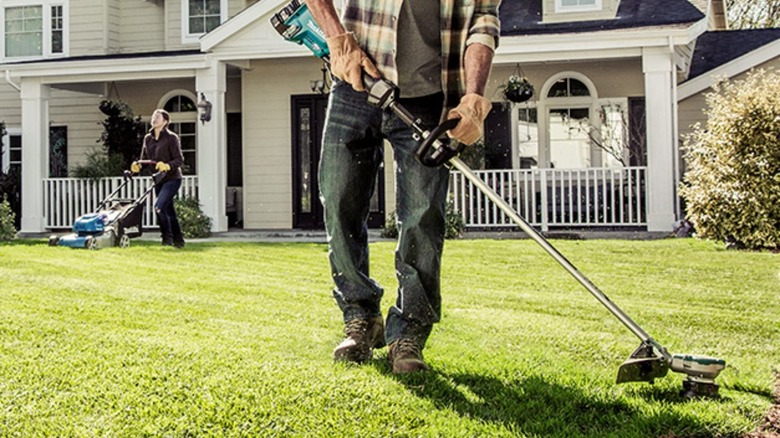 Man using a weed eater and another person mowing the yard