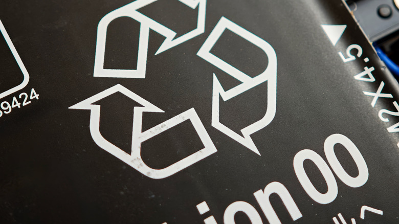 A recyling symbol printed on the black surface of a laptop in white innk
