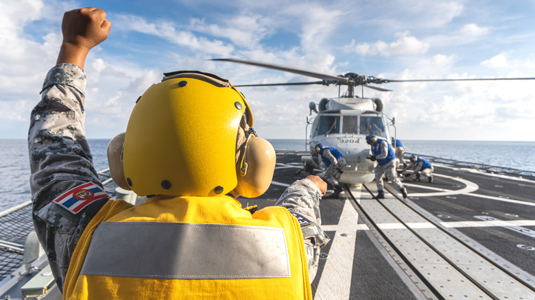 Navy shipboard flight crew landing MH-60S helicopter on ship's flight deck